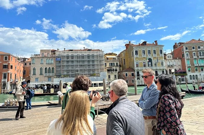 A guide talking to a small group on a stone quay beside the Grand Canal on a sunny day