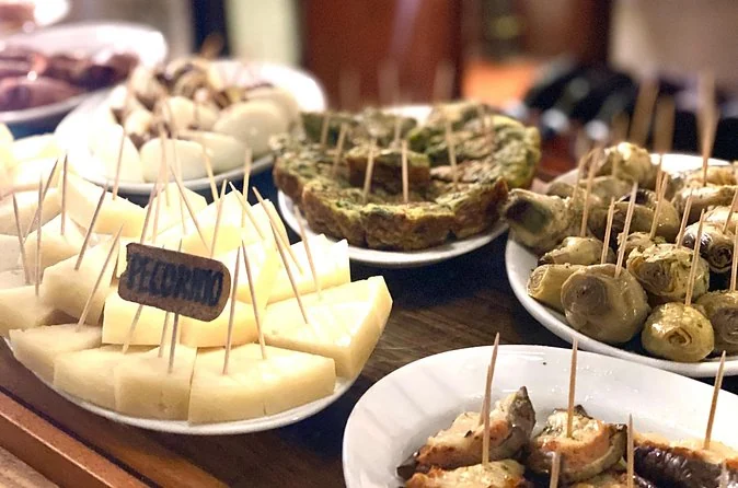 Teller mit Cicchetti auf einem Bartresen: Käse, gefülltes Gemüse und kleine Spieße mit handgeschriebenen Schildern