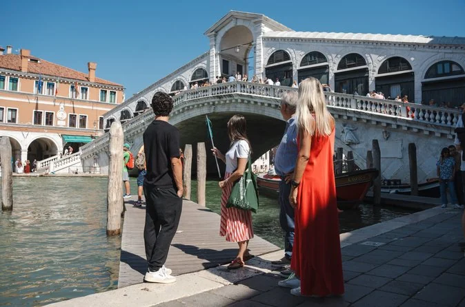 Visitors standing on the quay at the foot of the Rialto Bridge looking up at its arch